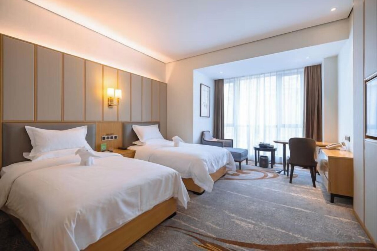 A hotel room with two beds, a desk, a chair, a small table, and a window with curtains.