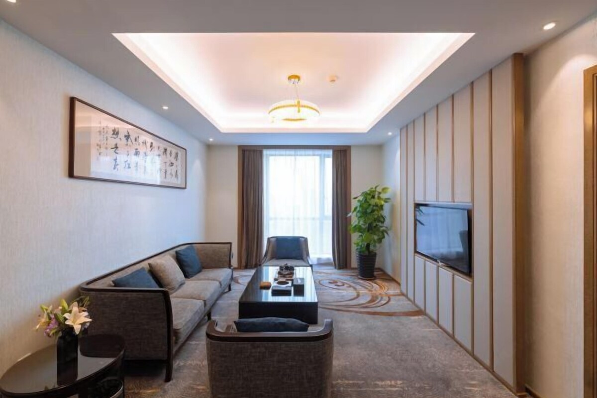 A modern hotel room with a sofa, a coffee table, a TV, and a large window.