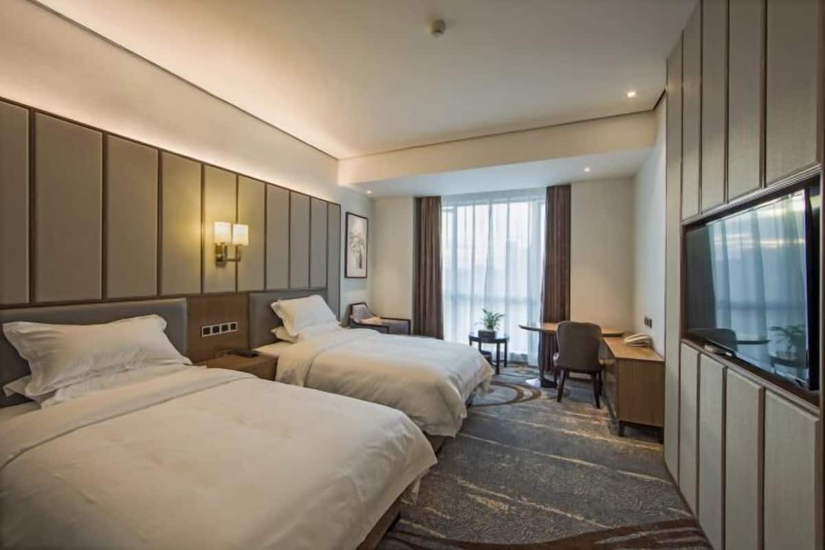 Une chambre d’hôtel avec deux lits, un bureau, une chaise, une télévision et une fenêtre avec des rideaux.