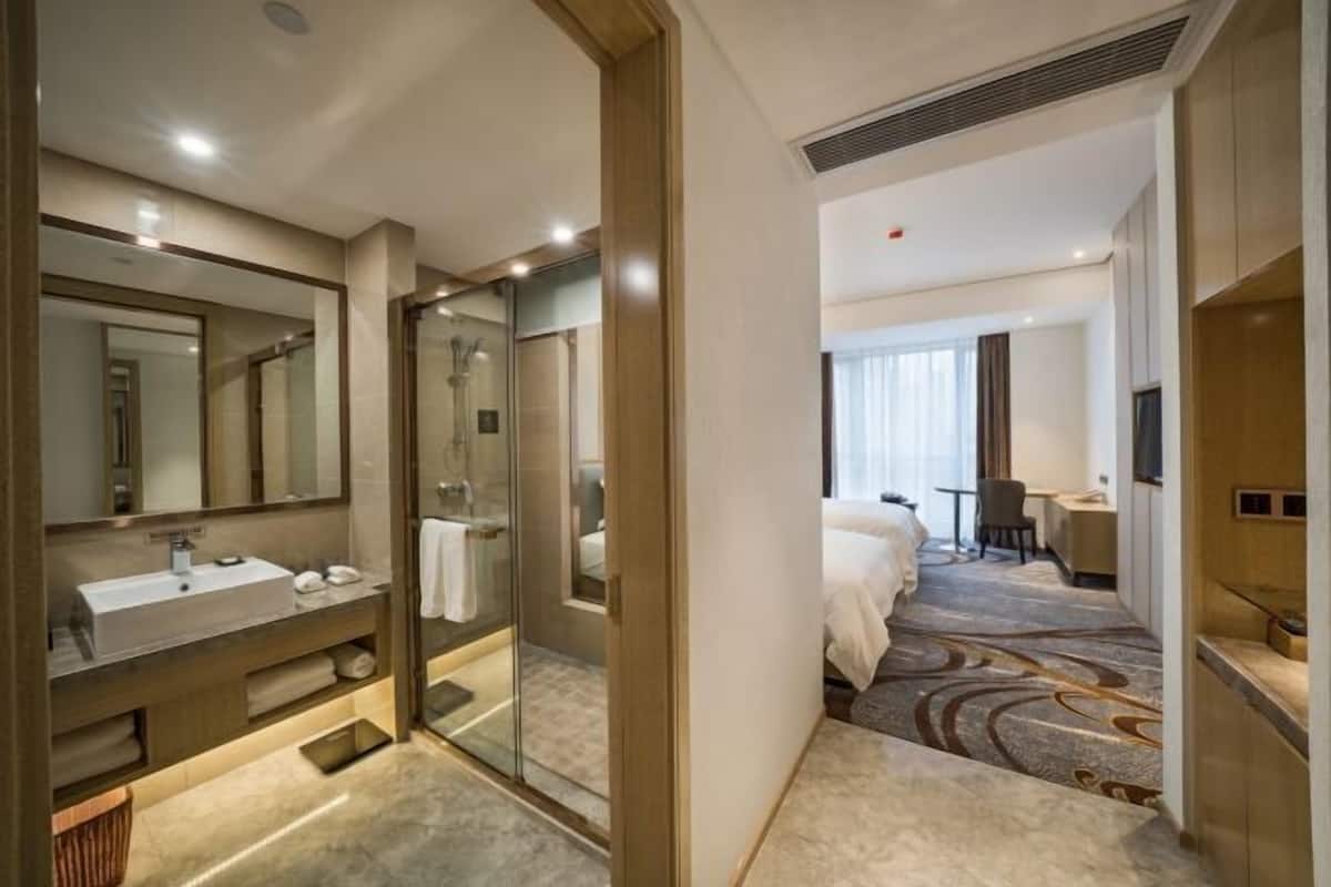 Une chambre d’hôtel équipée d’un grand miroir, d’un lavabo, d’une douche, d’un lit, d’un bureau et d’une télévision.