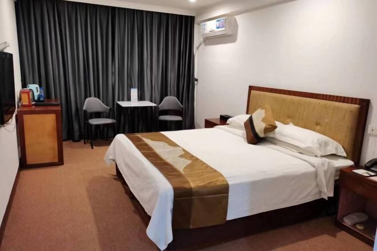 A hotel room with a bed, a desk, two chairs, a small table, and a curtain.