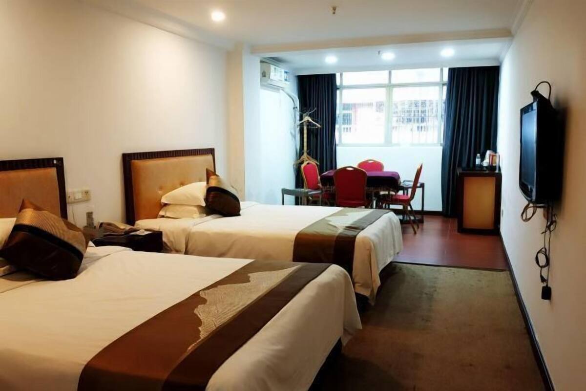 A hotel room with two beds, a desk, a chair, a TV, and a window with curtains.