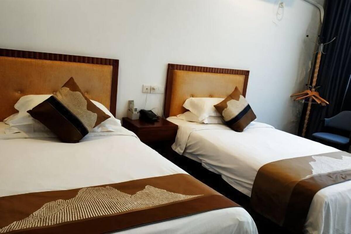 A hotel room with two beds, each with a headboard, bedside tables, and a hanging coat rack.