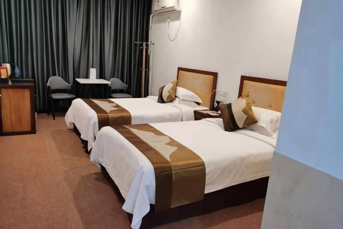 A hotel room with two beds, a desk, a chair, and a curtain.
