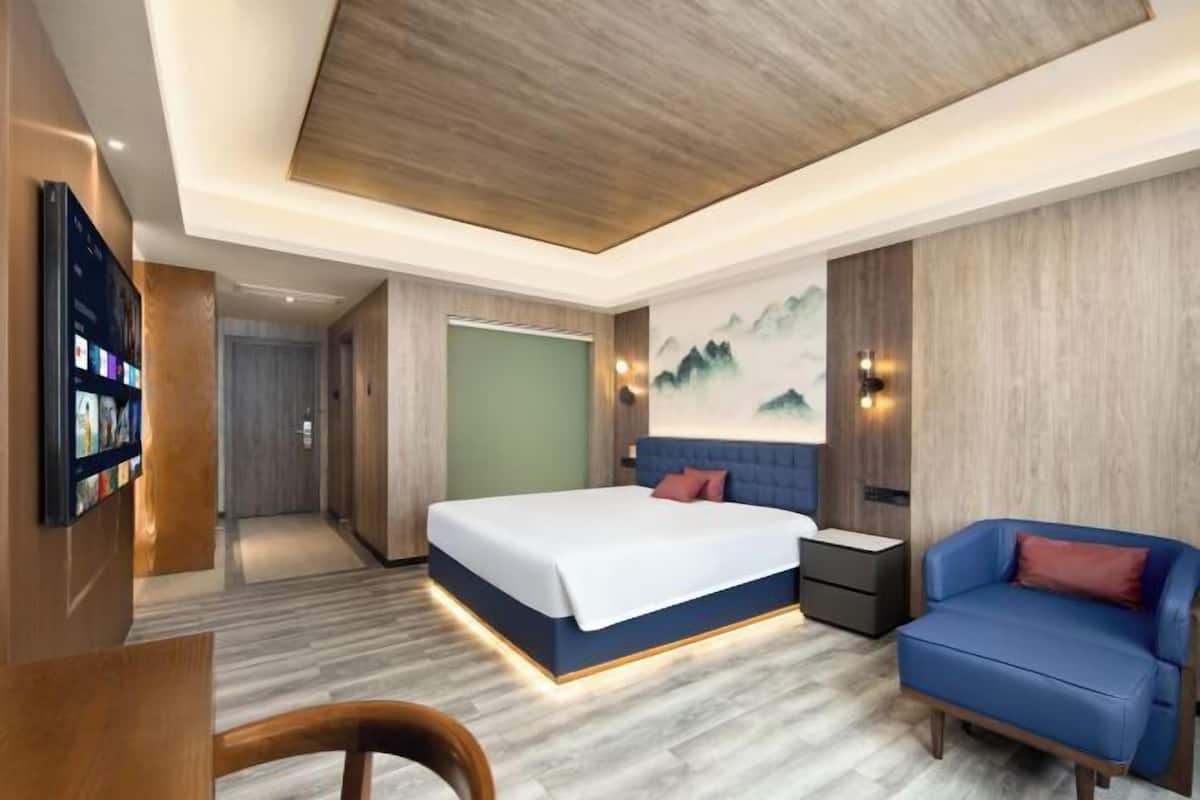 A modern hotel room with a large bed, a seating area with a blue sofa, a flat-screen TV, and a wooden ceiling.