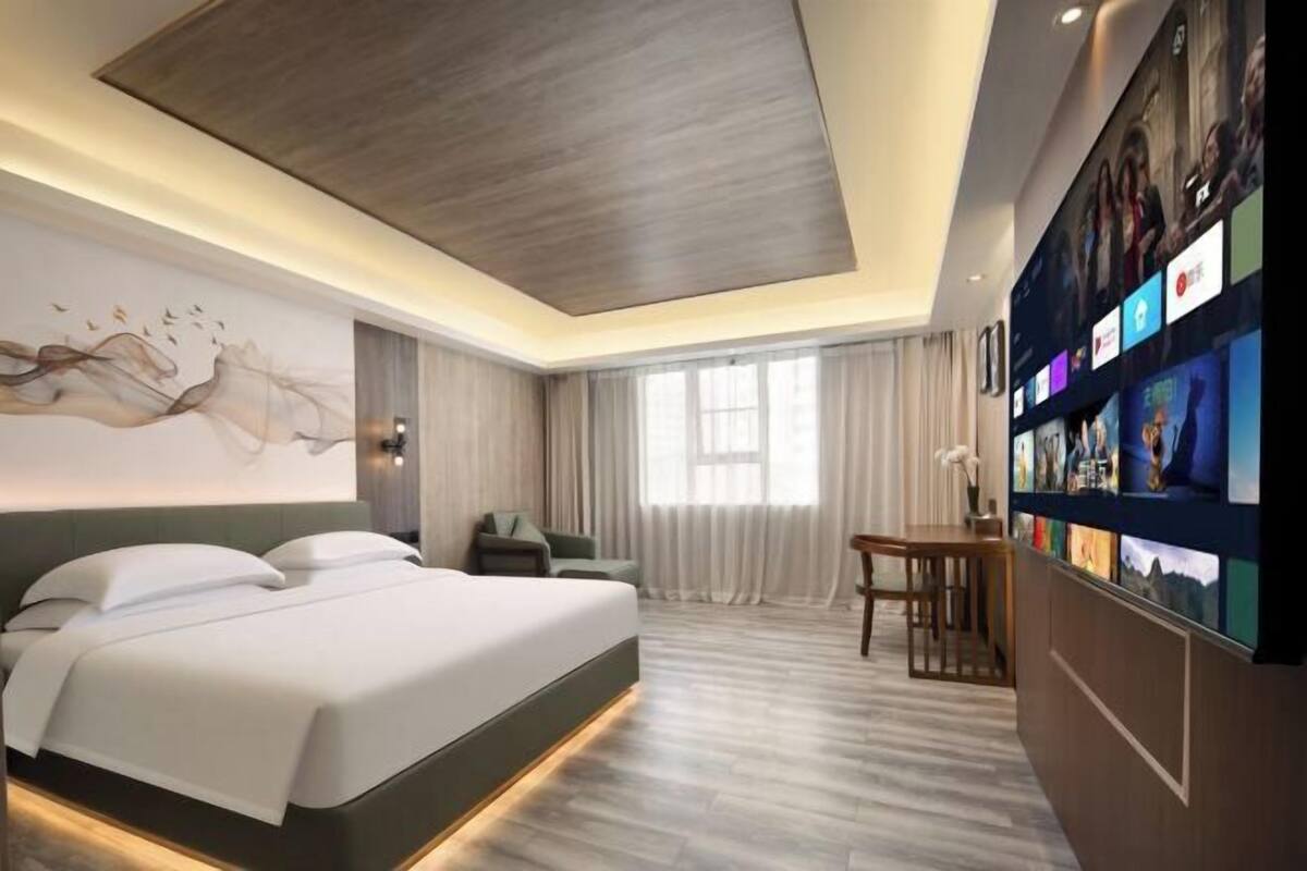 A modern hotel room with a large bed, a desk, and a wall-mounted TV.