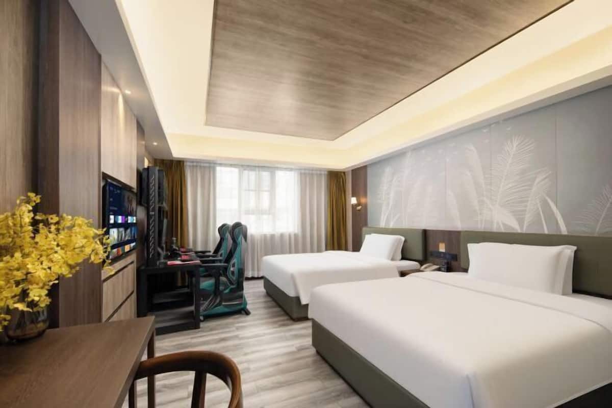 A hotel room with two beds, a desk with a chair, a TV, and a decorative plant.
