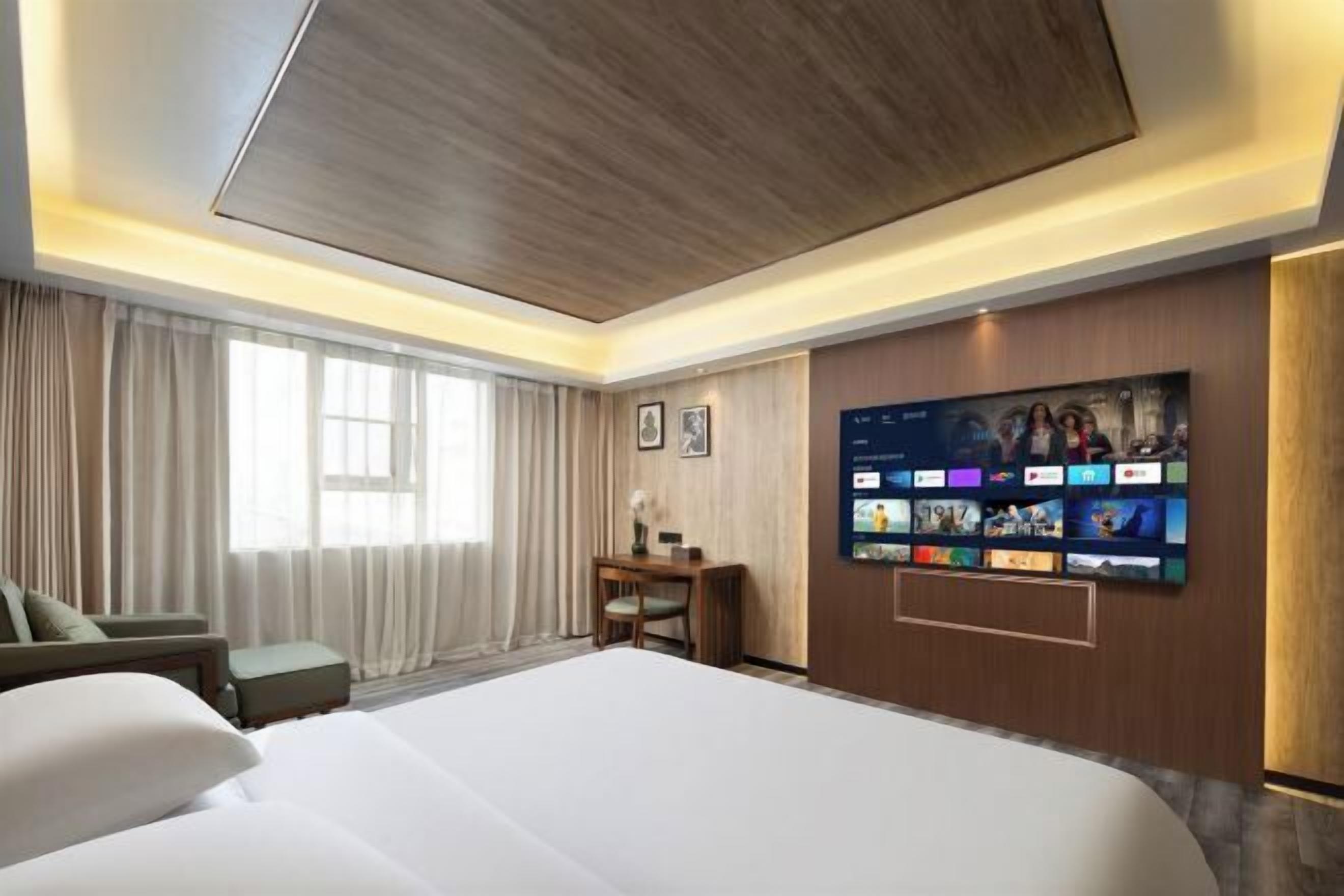 Hotelkamer met een groot bed, een bureau, een stoel en een wandtelevisie waarop verschillende zenders worden getoond.