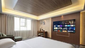 Hotelkamer met een groot bed, een bureau, een stoel en een wandtelevisie waarop verschillende zenders worden getoond.