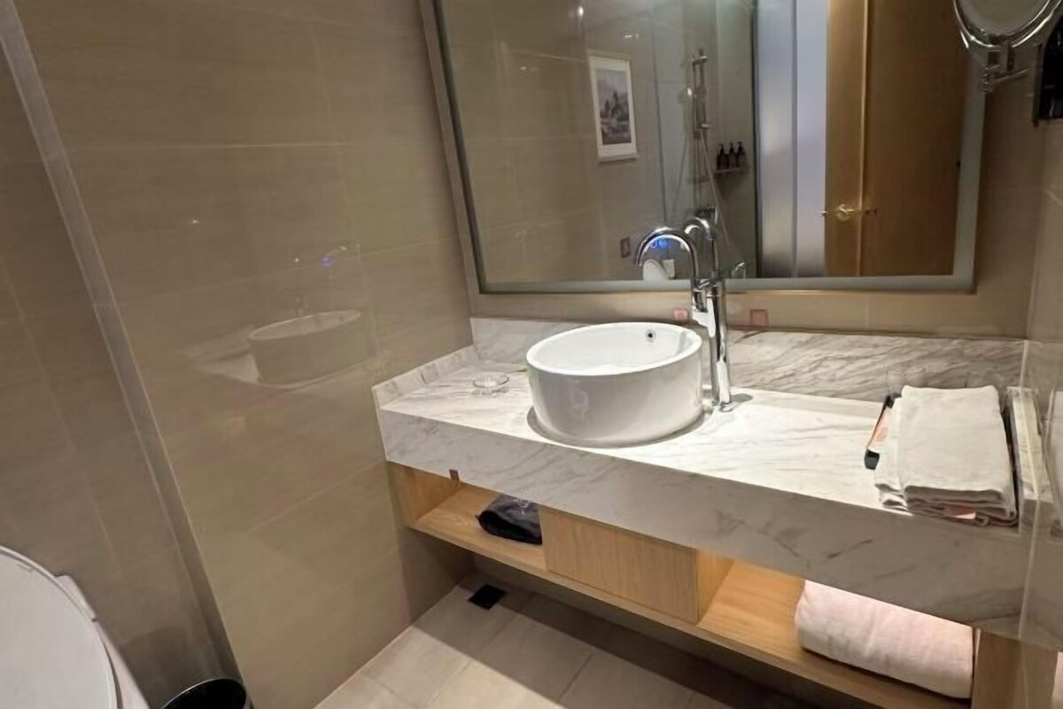 Un baño moderno con tocador de mármol, un espejo grande y zona de ducha.