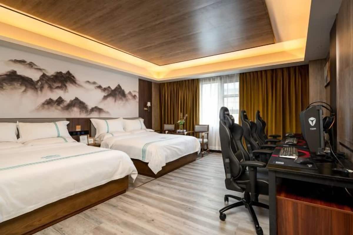 A hotel room with two beds, a desk with a computer, and a gaming chair.