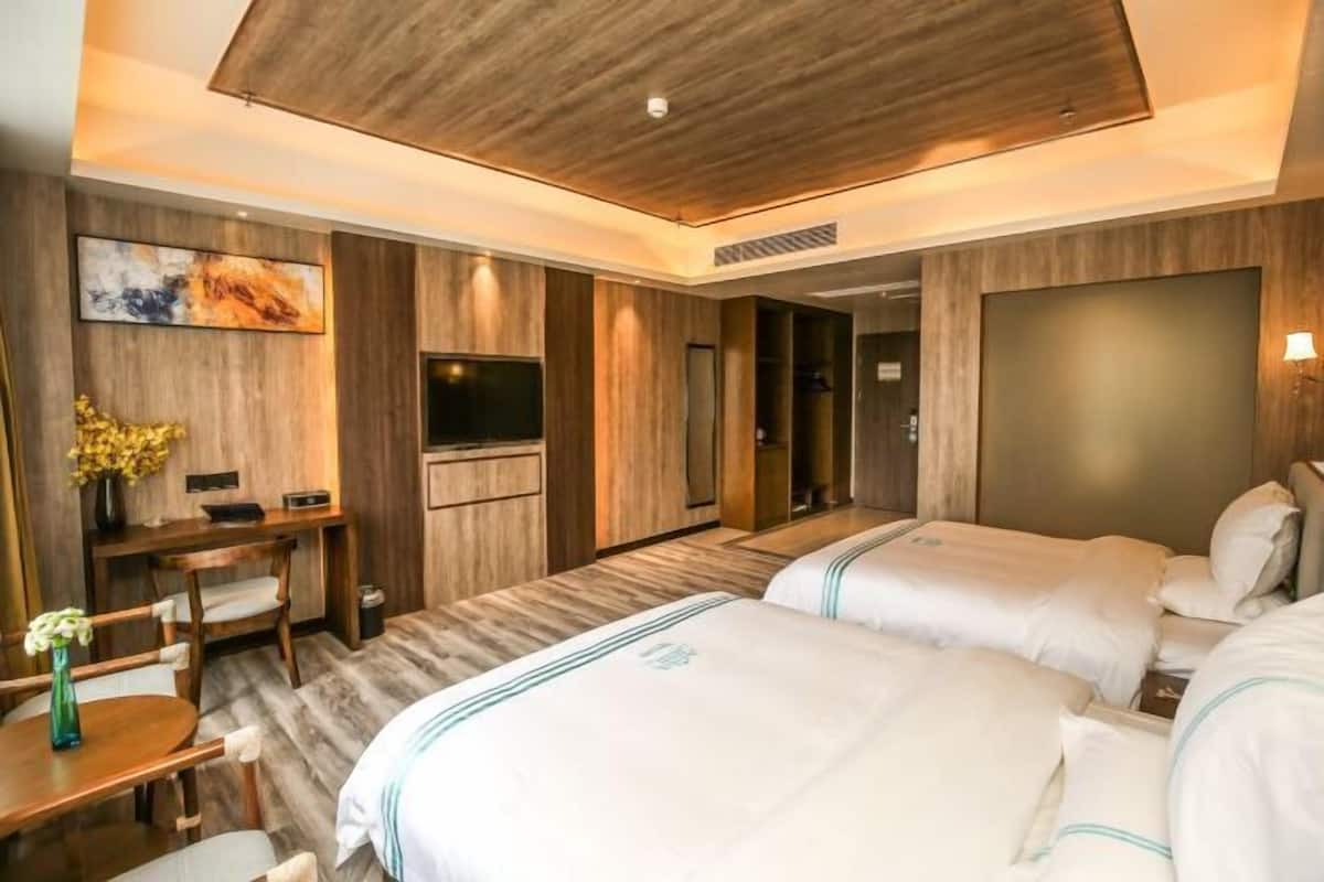A hotel room with two beds, a desk, a TV, and a painting on the wall.