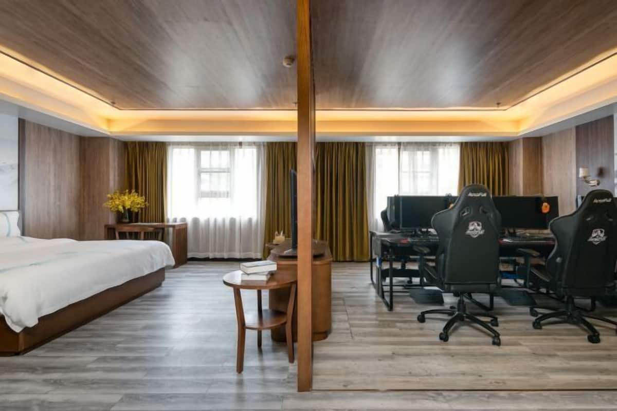 A hotel room with a bed, desk, chairs, and a television.