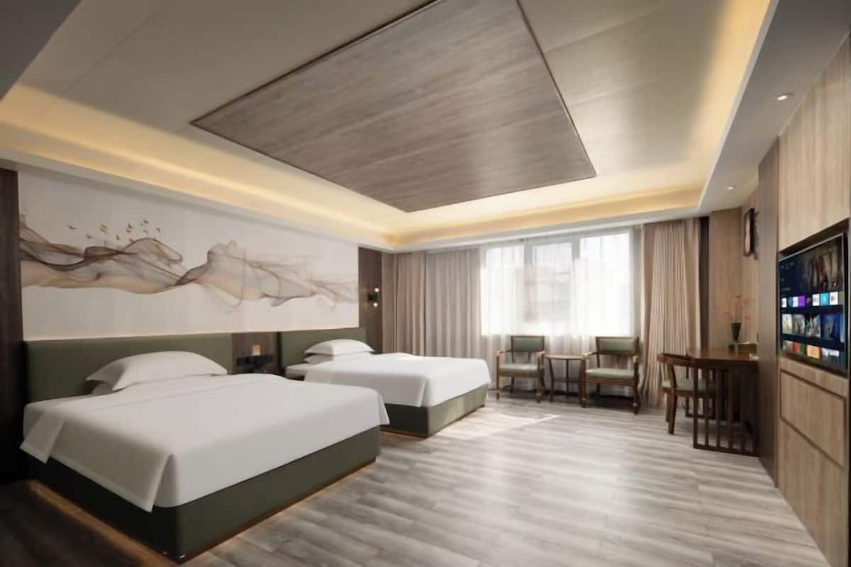 A hotel room with two beds, a dining area with chairs, a TV, and a large abstract wall art.