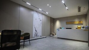 Zona reception di un hotel con parete in marmo, banco reception e area salotto con una poltrona.