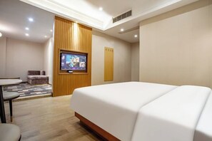Une chambre d’hôtel avec un grand lit, un téléviseur fixé au mur, un petit coin salon et un mur décoratif en bois.