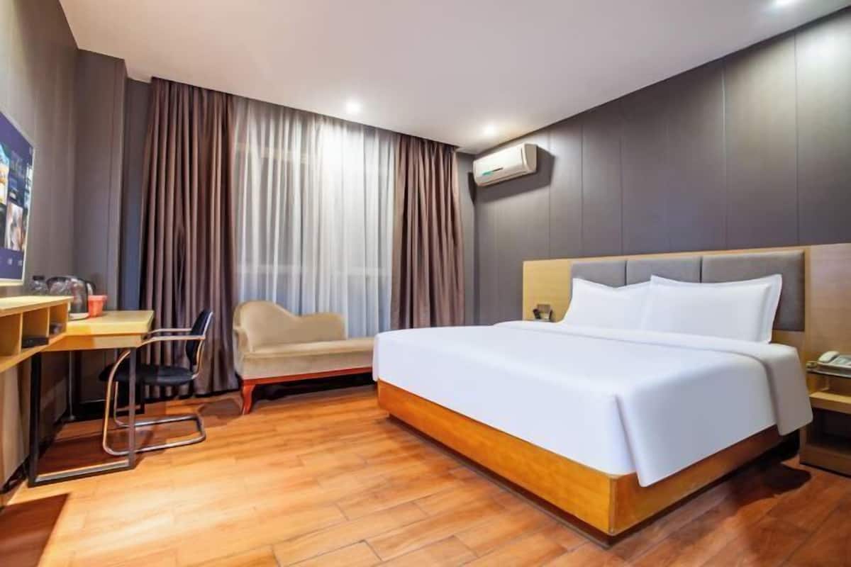 A hotel room with a bed, desk, chair, and curtains.