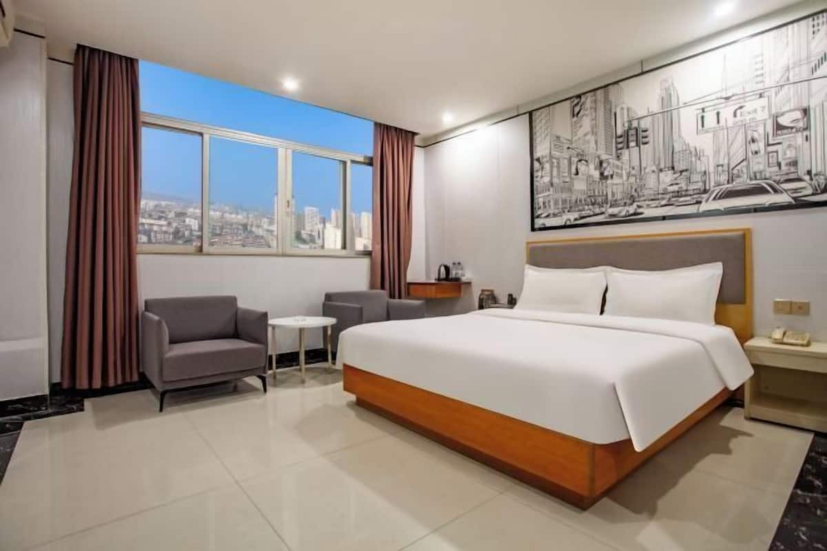A hotel room with a large bed, a sofa, a small table, a nightstand, and a cityscape view.