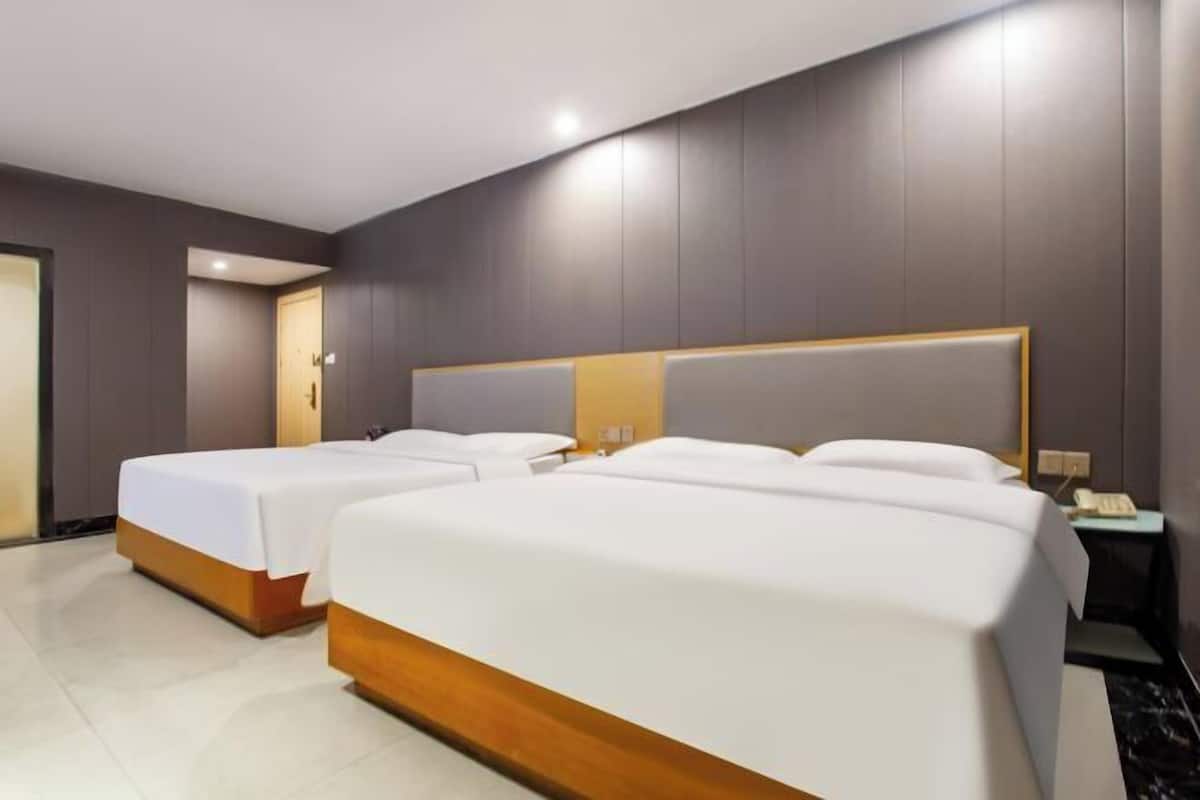A hotel room with two beds, a wooden headboard, a nightstand, and a door.