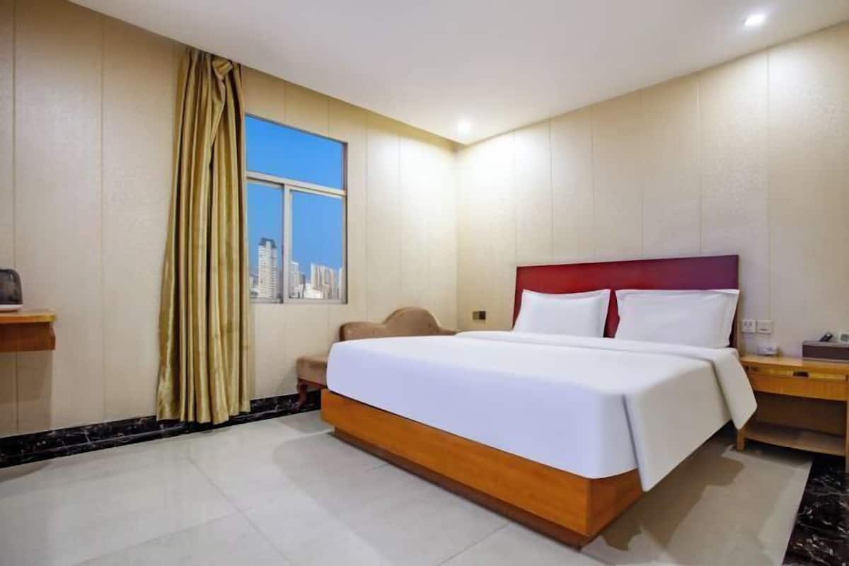 A hotel room with a bed, a nightstand, a chair, a window with curtains, and a cityscape view.