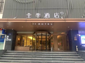 A hotel entrance with a revolving door, a signboard with hotel name, and a KETING bank branch nearby.