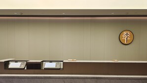 Uma mesa de recepção com um quiosque digital, uma placa na parede com caracteres chineses e um balcão de mármore.