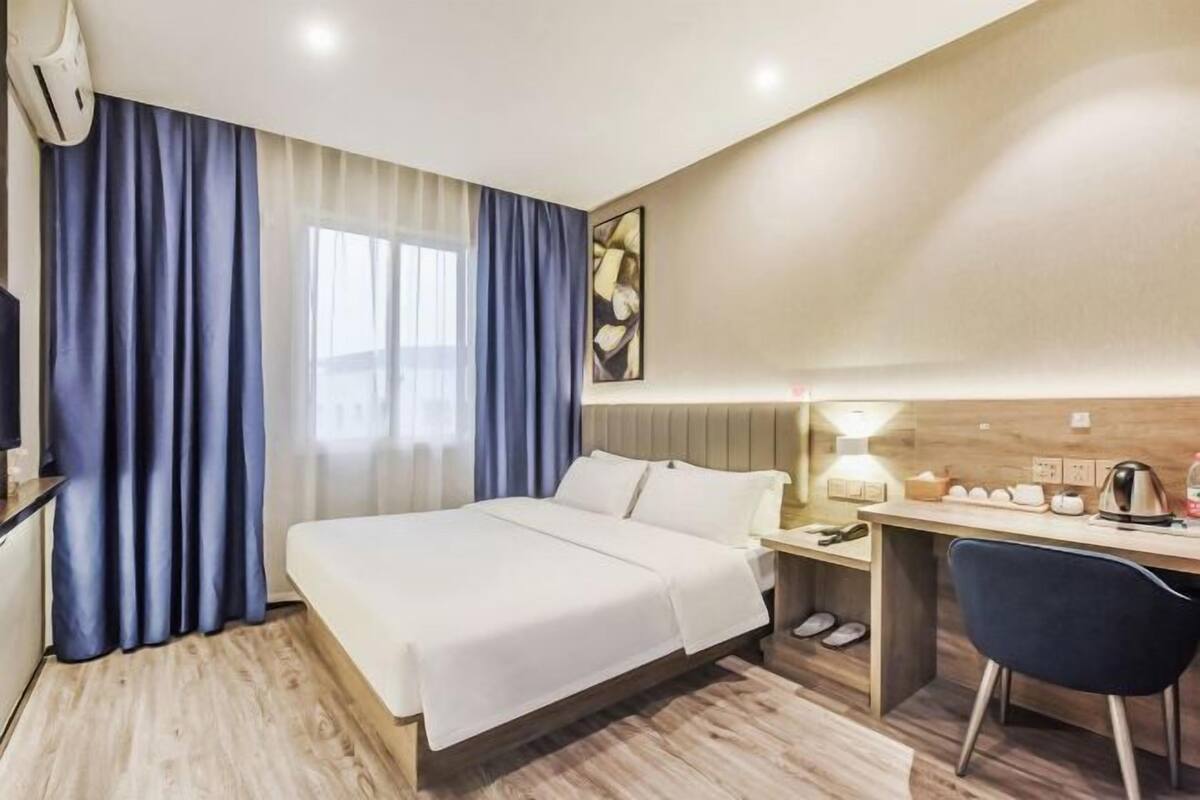 A hotel room with a bed, desk, chair, and a window with curtains.