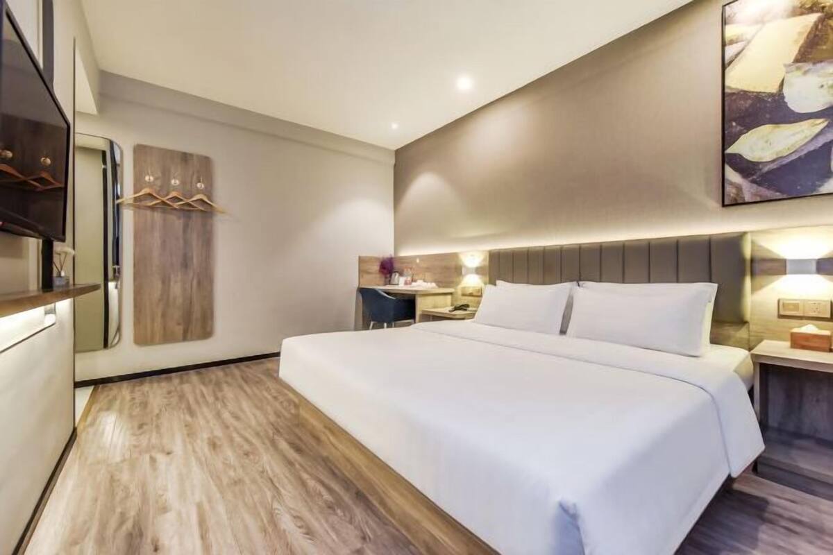 A modern hotel room with a large bed, a wooden floor, a desk with a chair, and a wall-mounted TV.