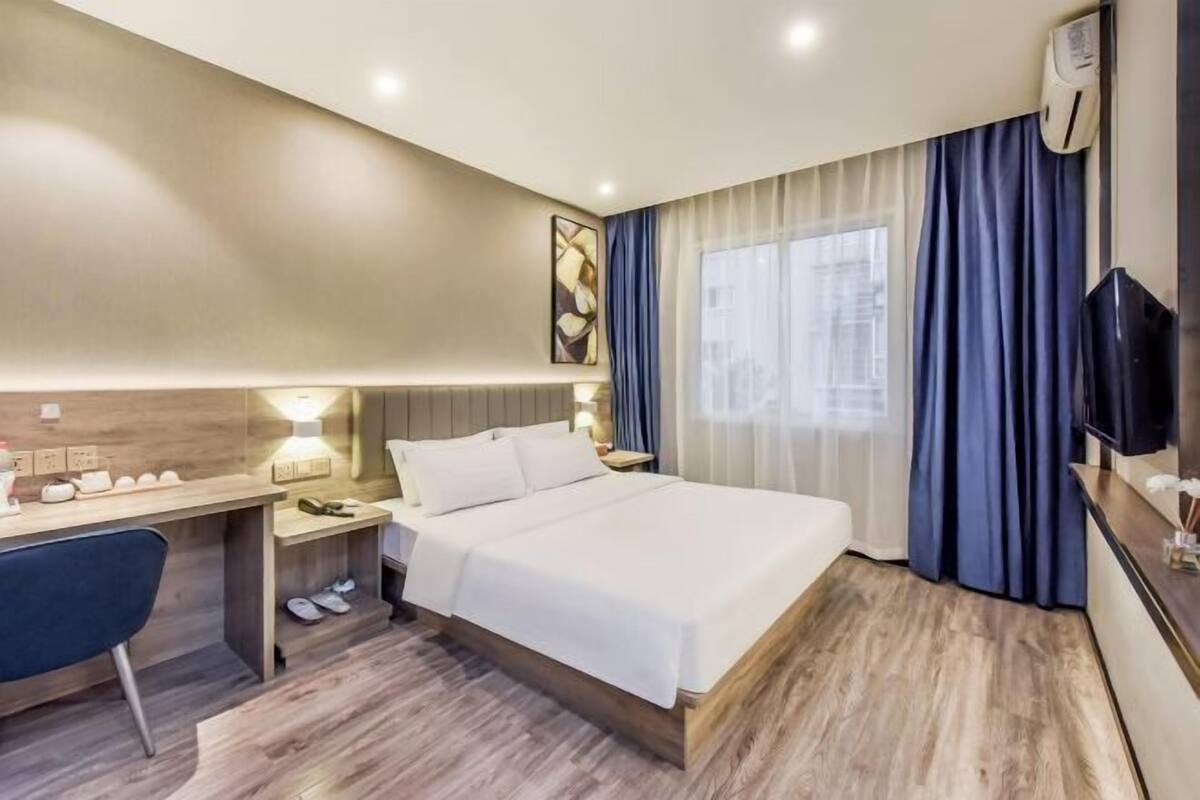 A hotel room with a bed, desk, chair, and a TV.