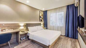 Quarto de hotel com cama, escrivaninha, cadeira e televisão.