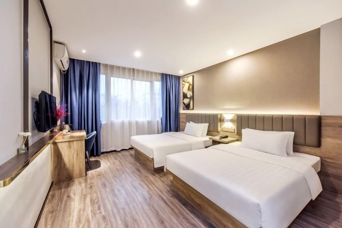 A hotel room with two beds, a desk, a TV, and a window with curtains.