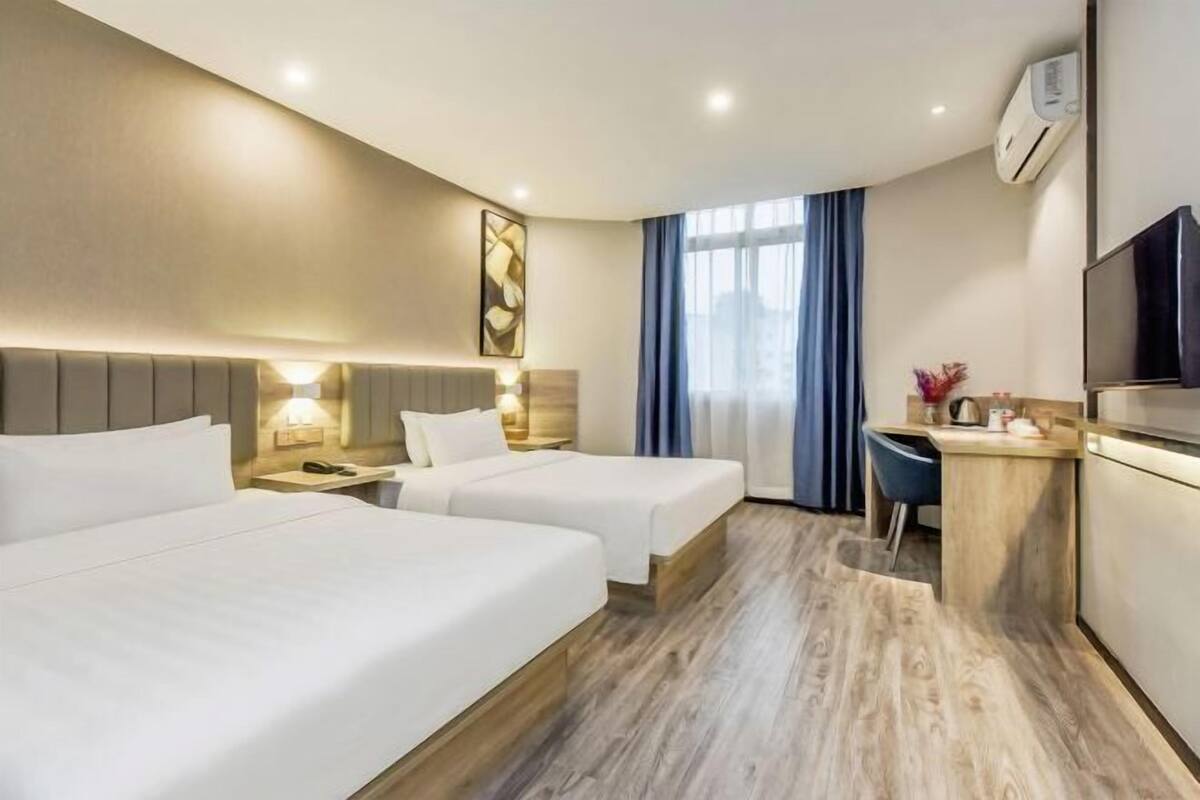 A hotel room with two beds, a desk, a TV, and a window with curtains.