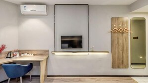 Une chambre d’hôtel moderne équipée d’un téléviseur à écran plat fixé au mur, d’un bureau en bois avec une chaise et d’un miroir avec un cadre en bois.