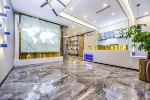Eine moderne Hotelhalle mit Marmorboden, einer Rezeption, einer Weltkarte und einem Bücherregal.