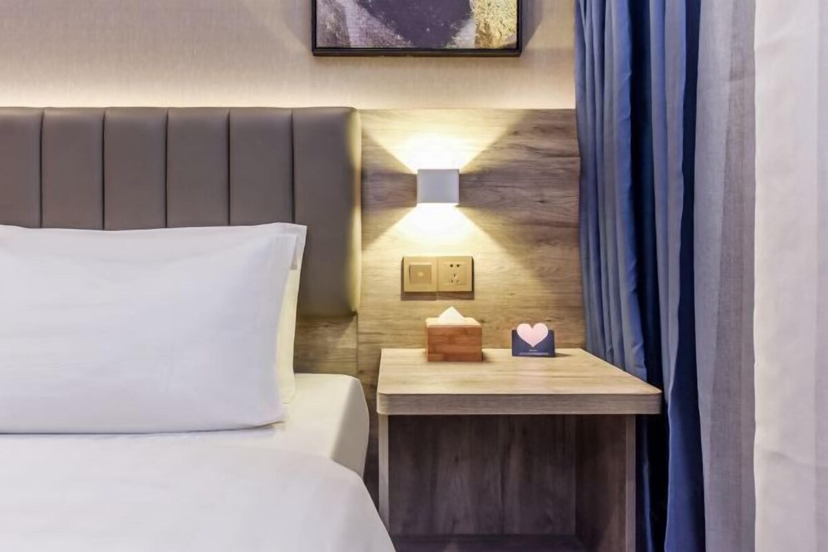 Habitació d'hotel amb un llit, una taula de nit amb una làmpada, una caixa de mocadors i una targeta.