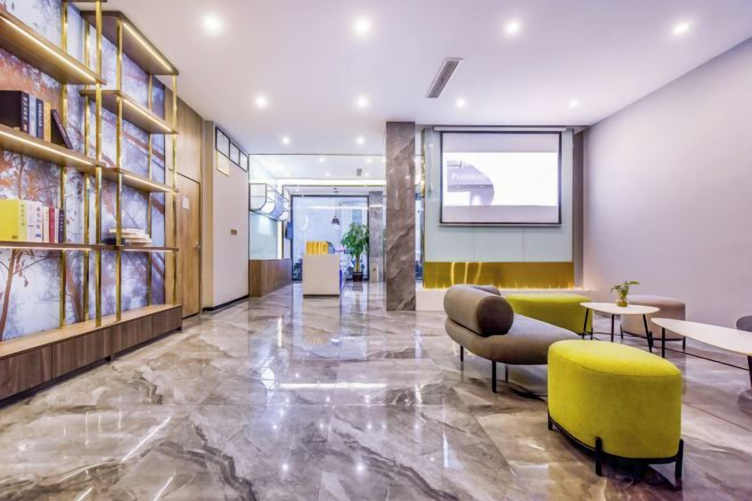 A hotel lobby with a marble floor, seating area with yellow chairs, a reception desk, and a bookshelf.