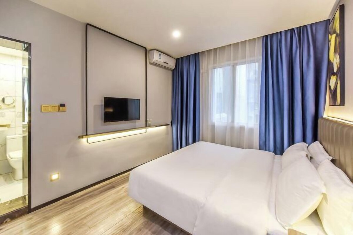 Una habitació d'hotel moderna amb un llit, una televisió de pantalla plana penjada a la paret i un bany visible a través d'una porta de vidre.