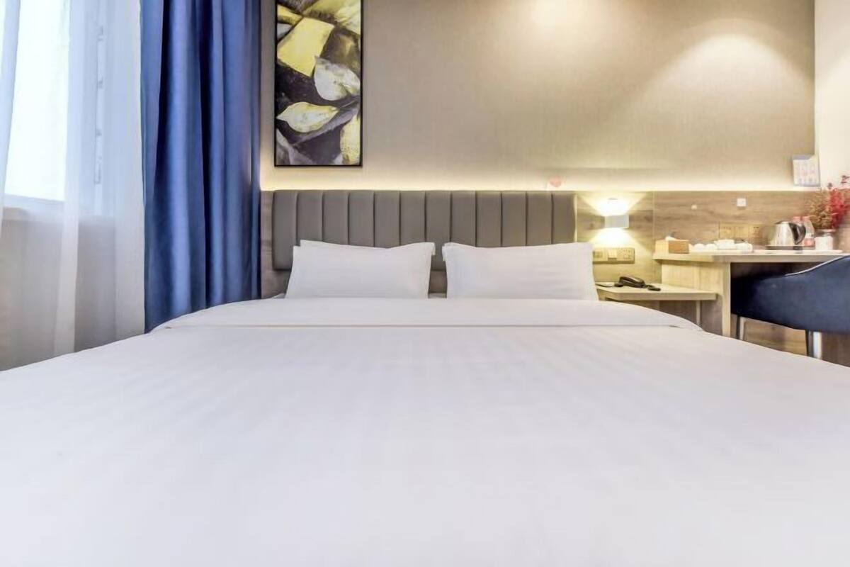 A hotel room with a bed, a desk, a chair, a nightstand, a lamp, and a painting on the wall.