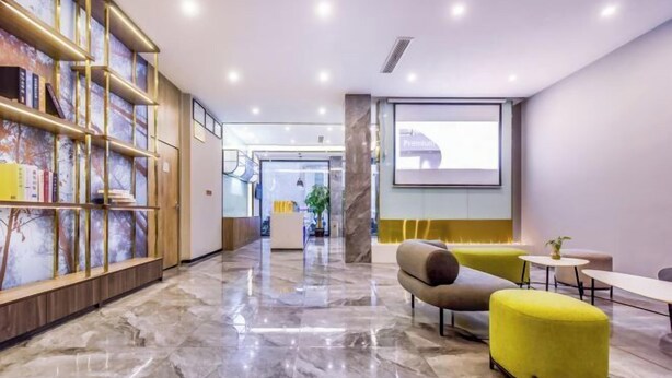 Un hall d’entrée moderne avec un sol en marbre, un comptoir d’accueil et un espace détente doté de canapés jaunes et gris.