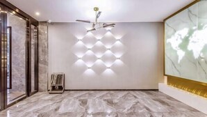 Une chambre d’hôtel moderne avec un sol en marbre, un ventilateur de plafond, un luminaire fixé au mur et un grand tableau abstrait.