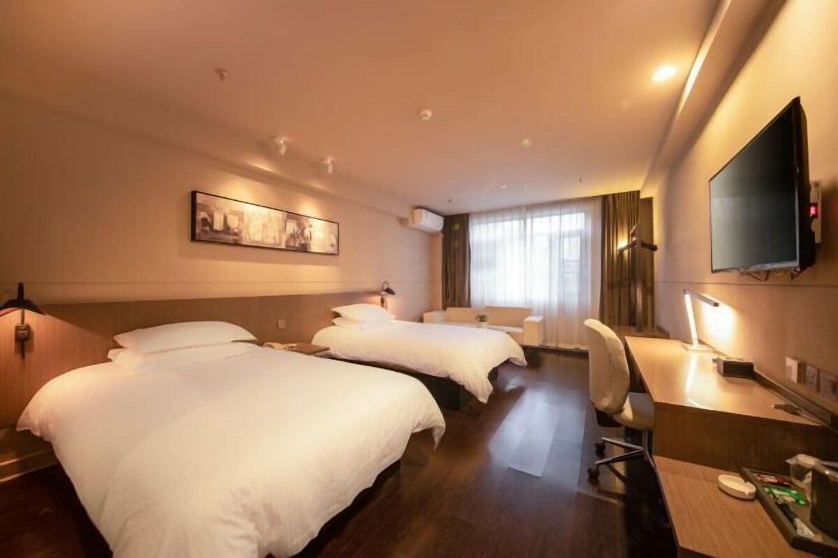 Habitación de hotel con dos camas, un escritorio, una silla, un televisor y una ventana con cortinas.