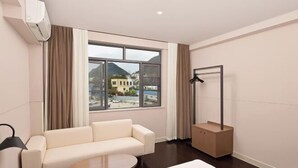 A hotel room with a sofa, a round table, a bed, a window with curtains, and a coat rack. - Jinjiang Inn Style (Huaxi District Xiahe Vanke Metropolis Store GuiyangGuizhou) (Guiyang)