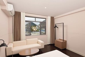 Habitación de hotel con sofá, una mesa redonda, cama, ventana con cortinas y perchero.
