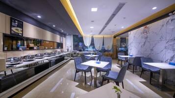 A modern restaurant with a buffet area, multiple dining tables, and a view of a building through a window.