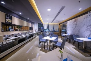 A modern restaurant with a buffet area, multiple dining tables, and a view of a building through a window. - Jinjiang Inn Style (Huaxi District Xiahe Vanke Metropolis Store GuiyangGuizhou) (Guiyang)