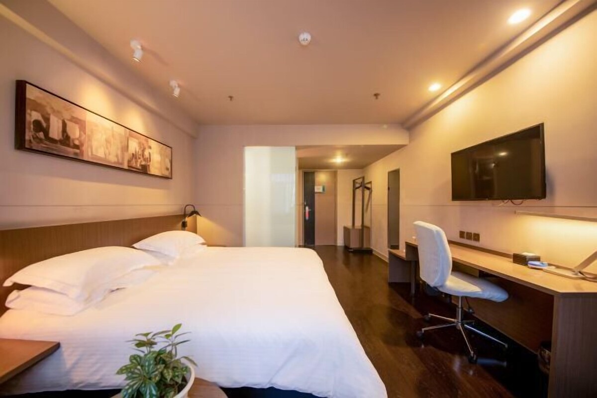 Habitación de hotel con cama, escritorio, silla, televisor y cuadros en la pared.