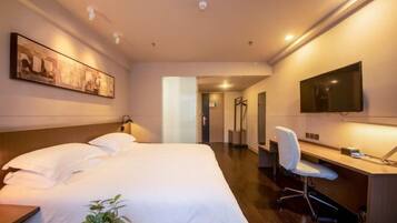 A hotel room with a bed, a desk, a chair, a TV, and artwork on the wall.