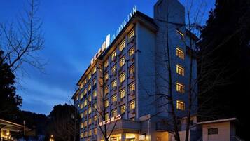 A multi-story hotel building with a prominent signage at the top, a well-lit facade, and a parking area in the foreground.