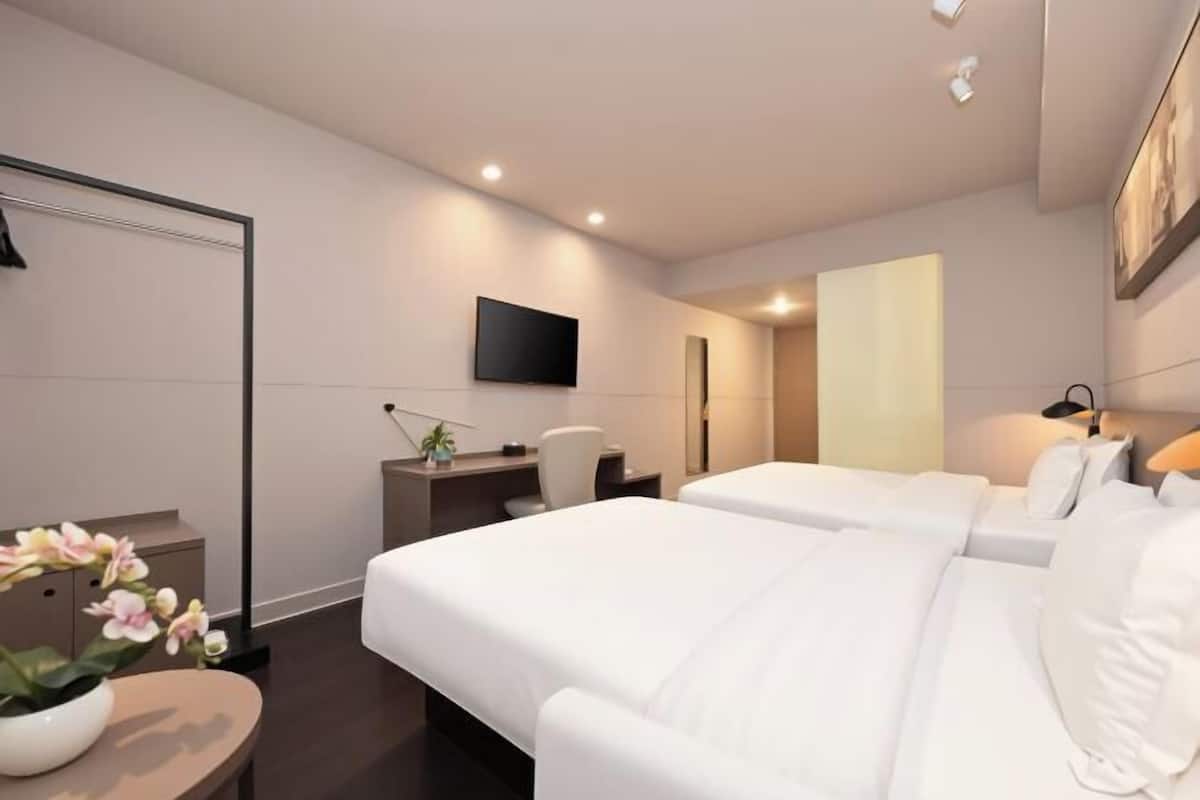 A hotel room with two beds, a desk, a chair, a TV, and a mirror.