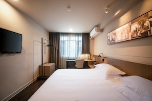 Habitación de hotel con una cama grande, un escritorio, una silla y un televisor en la pared.